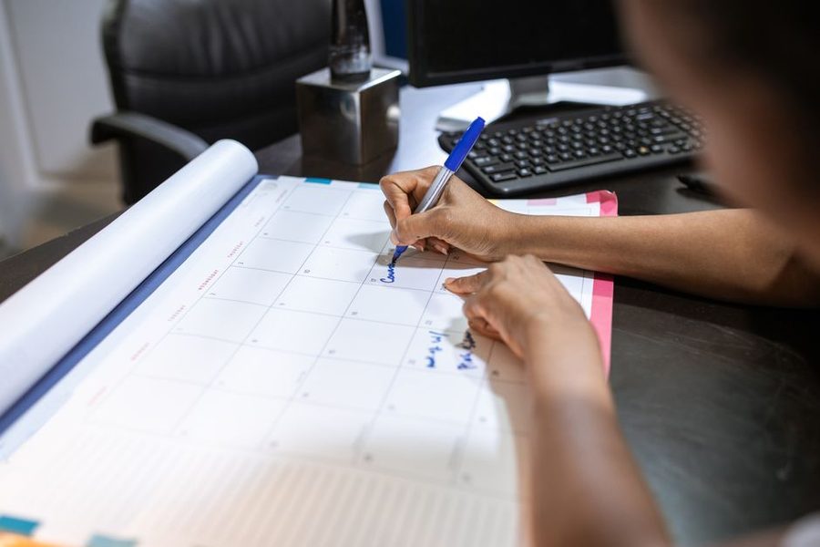 Mulher anotando uma data em um calendário de mesa ao lado do teclado